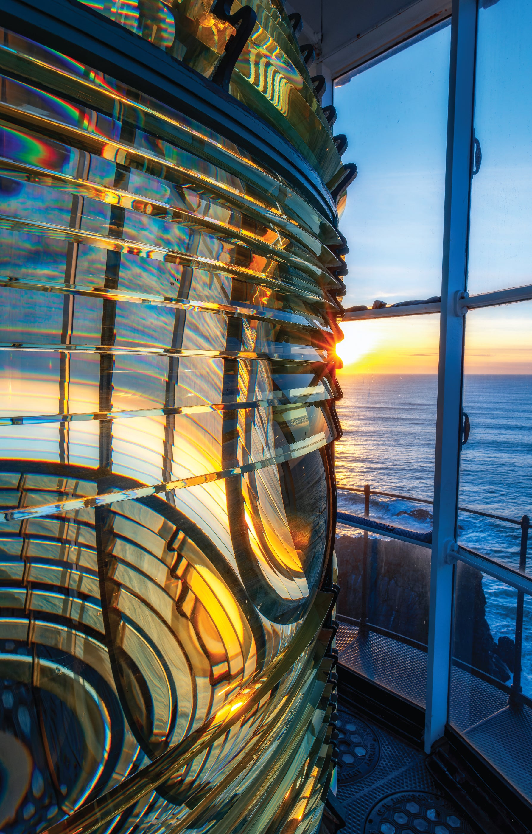 Inside the lantern room of Yaquina Head Lighthouse, the antique Fresnel lens glowing with sunset light.